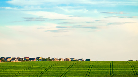 Green field with tractor tracks in the background of village houses. Agricultural background with tractor ruts.の写真素材