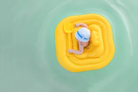 Baby floats in a yellow inflatable raft. Small child in yellow rubber ring swims in open water. View...
