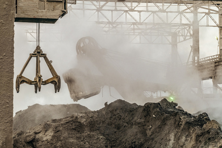 Industrial background. Loading equipment in hot slag dust of heavy metallurgical industry. Excavator and grapple grab of overhead crane in a dirty outdoors industrial plant shop.の写真素材
