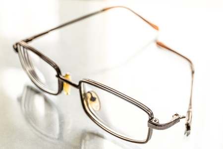 Eyeglasses with a broken handle on a bright background. Limited depth of field.