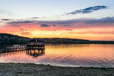 Footbridge with a gazebo on the lake shore in light of the low evening sun. Sunset and quiet nature.の写真素材