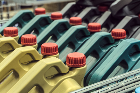 Colored plastic cans with engine oil. Rows of canisters placed on a pallet. Limited depth of field.
