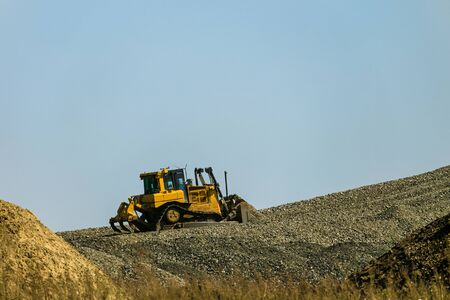 Motorized bulldozer raking rubble piles to uphill. Road building industry.