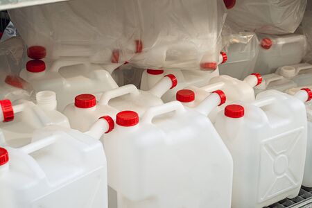 Empty white plastic cans with red lids on a rack. Domestic drinking water tanks.の写真素材