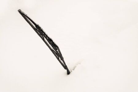 Snow covered front car window glass. Icy Ñar wiper sticking out of snow. Winter weather...