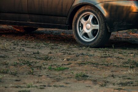 Black car stands on dry clay soil with sparse stunted vegetationの写真素材