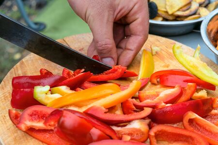 Knife slicing red and yellow sweet peppers on wooden cutting boardの写真素材