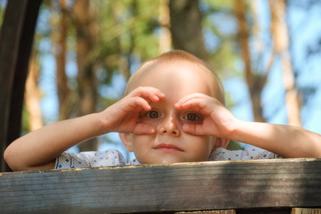 Child looking in hands like through binoculars. Boy on outdoors playground.の写真素材