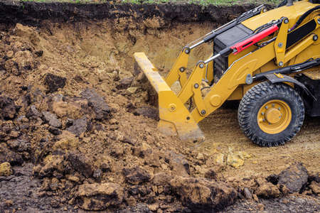 Loader excavator with backhoe planning and cutting clay ground at eathmoving works in construction...