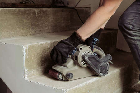 Grinding concrete staircase surfaces with an electric sander. Worker woman with hand tool grinding machine.の写真素材