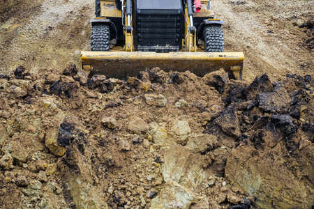 Tractor with backhoe for earthmoving works in construction site pit. Front view. Moving soil in the pit.の写真素材