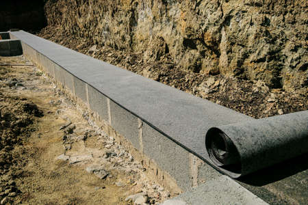 Long line of rolled bitumen waterproofing material in two layers lies on the masonry of concrete...