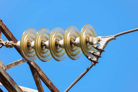 Transparent high voltage insulator garland with electric wire on blue sky background. Electric power...