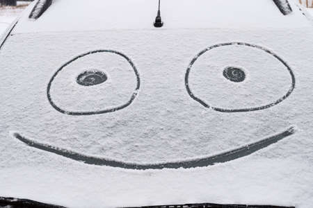 Snow covered windshield with drawn smile face. Close-up.