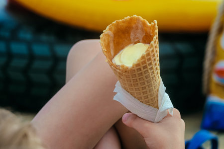 A bitten waffle ice cream cone in the hands of a childの写真素材