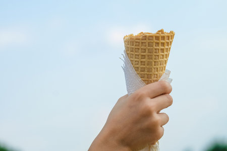 Rised up a waffle cone in the hand of a child on the sky backgroundの写真素材