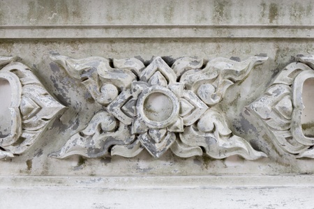 An old white concrete wall which has carved with Thai style pattern art. 