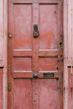 Old vintage english style red salmon pink front door with age related marks brass knocker doorknob banham security lock and letterboxの写真素材