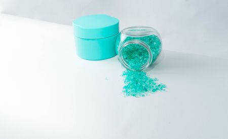 Bank with cream and bath salt in turquoise color lie on a white background. The can is on its side,...
