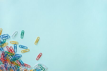 Horizontal close-up flat lay composition of multi-colored paper clips on a light blue background. A...
