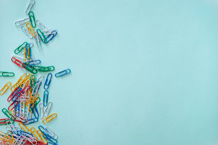 Horizontal close-up flat lay composition of multi-colored paper clips on a light blue background. A...