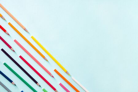 Multicolored pencils located diagonally in the lower left corner of the photo. Horizontal photo. Flat lay minimalistic composition on a light blue background. Office supplies concept. Back to school, college, education concept. Space for text, copy space. Stationery.の写真素材