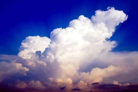 White fluffy clouds in blue sky with the rays of sun