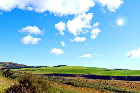 Sunshine on meadow hill with white clouds and blue sky