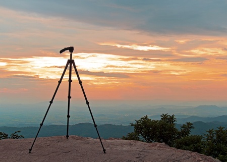 Silhouette of camera tripod standing on the top at sunsetの写真素材