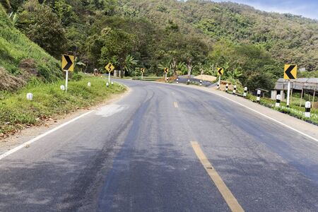 Asphalt road with road sings showing curves ahead on nature background