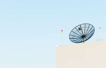 Satellite dish antenna mounted on rooftop in urban area on clear blue skyの写真素材