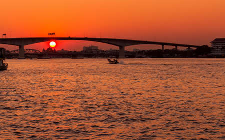Dramatic sunset on river with bridge and boat in Bangkok Thailandの写真素材
