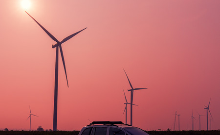 Wind turbines power generator with car on sunrise at farmer field