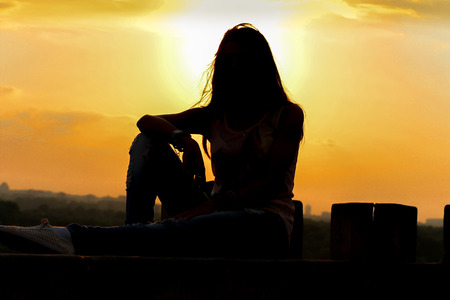 Silhouette of girl on beautiful sunset sitting on the top of the belvedereの写真素材