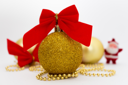 Gold shiny Christmas balls with red ribbon and pearls and little blured santa isolated on white backgroundの写真素材