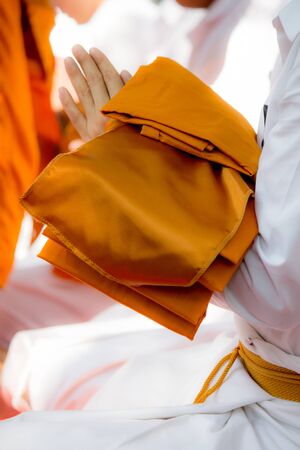 Person about to be ordained as a Buddhist priest carrying robe of Buddhist monk while putting the palms together in salute during ordination.の写真素材
