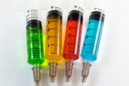 plastic medical syringes containing multicolor solutions with white backgroundの写真素材