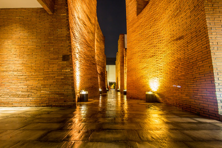 Ayutthaya Province,Thailand on August 20,2018:Night scene of the corridor lined with curved red brick walls at Sala Ayutthaya.With a glimpse of ancient pagoda of Wat Phutthaisawan at the end.のeditorial素材