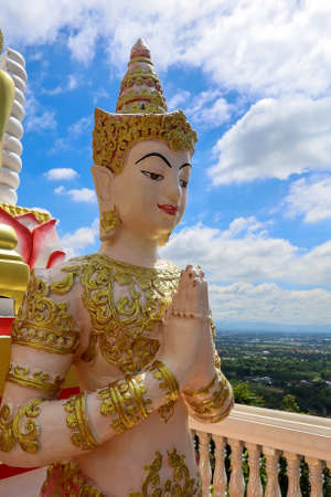 Mae Hia,Chiang Mai,Northern Thailand on Septemmber 13,2019:The figure of a deva clasping hands in token of worship in front of Reclining Buddha Statue at Wat Phra That Doi Kham.のeditorial素材