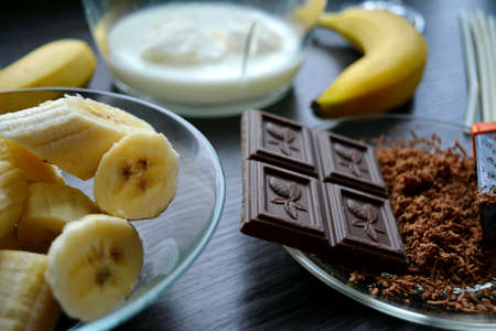 Preparation of a milkshake with banana and chocolate on a black wooden backgroundの写真素材