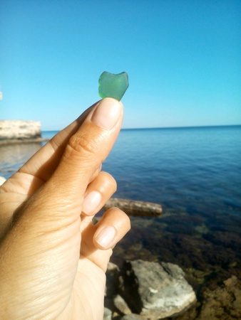 Green stone glass heart in the hand sea and blue sky backgroundの素材