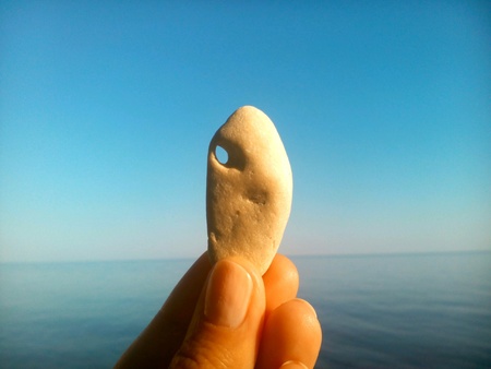 A stone with a hole in hid hand sea and blue sky backgroundの素材