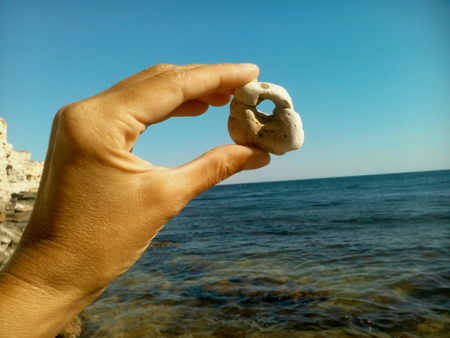 A stone with a hole in hid hand sea and blue sky backgroundの素材