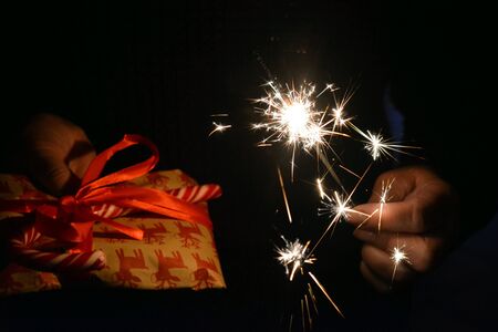 Christmas and New year gift and Bengal light in hands dark backgroundの素材