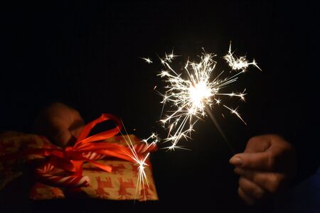 Christmas and New year gift and Bengal light in hands dark background