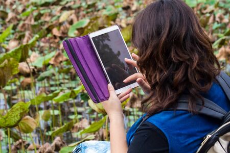 Woman sitting near the pond handle Tablet.の写真素材