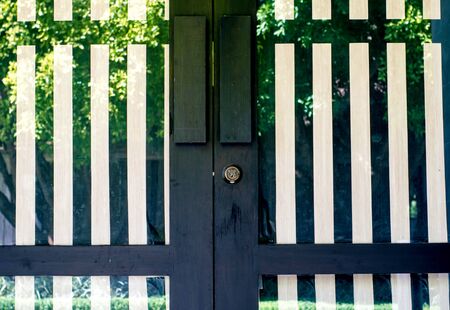 Door, black and white stripes made of metal and glass with green trees reflection.の写真素材