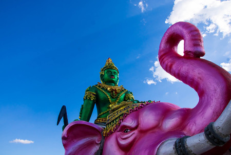 The green Indra statue sits on a pink elephant behind the clouds and the sky.の写真素材