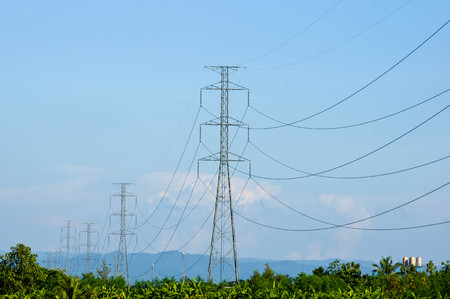 high voltage towers on green tree, against blue cloudy sky