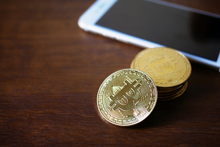 stack of Physical Bitcoins with smartphone virtual currency concept on wooden backgroundの写真素材